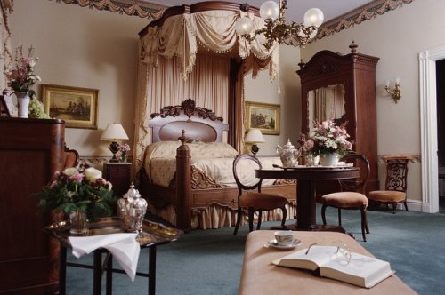 Elegant bedroom with a four-poster bed, vintage furniture, floral decor, and a cozy seating area.