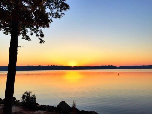 A serene sunset over a calm lake, with vibrant orange and yellow hues reflecting on the water's surface.