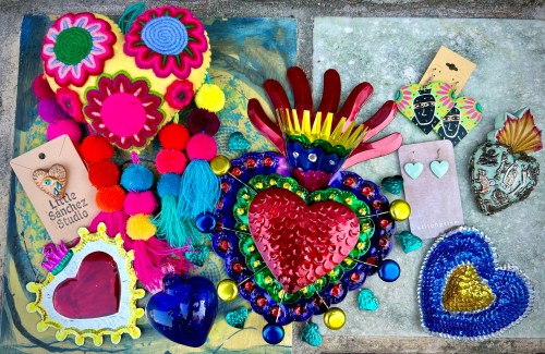 Colorful handmade crafts including hearts, pom-poms, and decorative tags arranged on a textured surface.