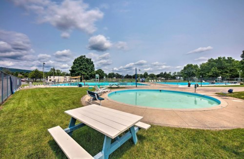 A sunny outdoor pool area with lounge chairs, grassy spaces, and multiple swimming pools under a partly cloudy sky.