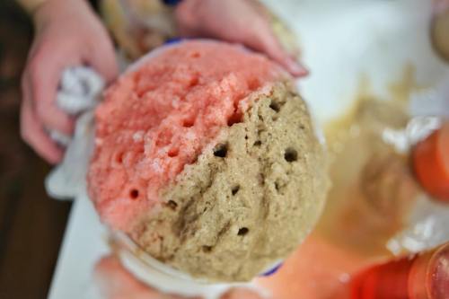 A person holding a large scoop of two-colored ice cream, pink and brown, with some melting around the edges.