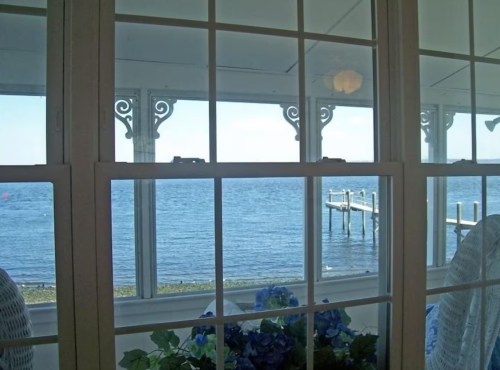 View of a serene waterfront through a window, featuring a dock and blue flowers in the foreground.