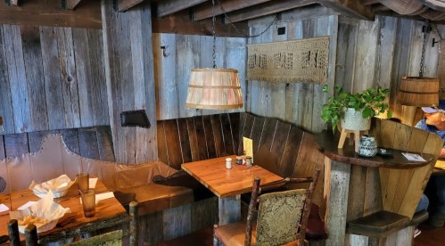 Cozy restaurant interior with wooden walls, a corner booth, and rustic decor, featuring a plant and warm lighting.