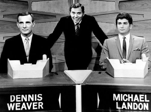 Black and white image of two men, Dennis Weaver and Michael Landon, seated at quiz show podiums with a host standing between them.