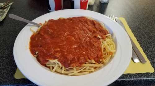 A plate of spaghetti topped with a rich tomato sauce, served with a fork on a patterned table.