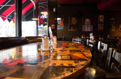 A cozy restaurant interior featuring a colorful table with photos and a view of large windows and artwork on the walls.