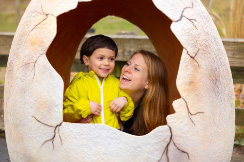 A woman and a young boy smile together while peeking out from a large, egg-shaped sculpture.