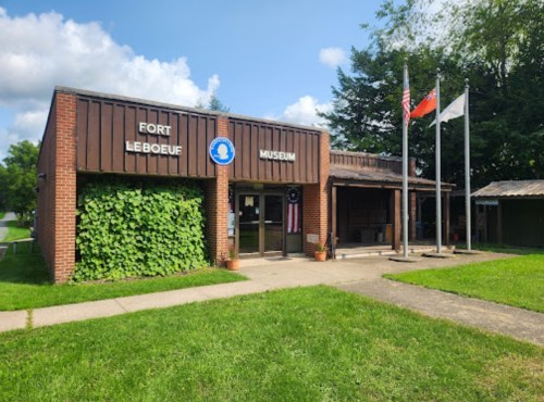 Exterior of Fort LeBoeuf Museum with flags, greenery, and a clear blue sky.