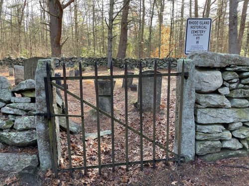 A wrought iron gate opens into a historical cemetery surrounded by stone walls and autumn leaves.