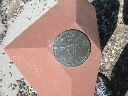 A metal survey marker on a red stone base, inscribed with "U.S. Department of the Interior" and location details.