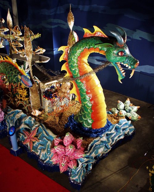 A colorful dragon float adorned with flowers and sea creatures, set against a blue backdrop.