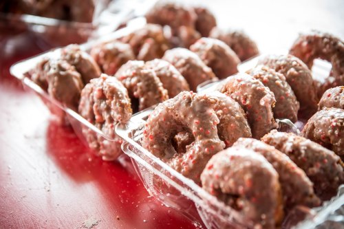 A close-up of trays filled with frosted donuts topped with colorful sprinkles, arranged neatly on a red surface.