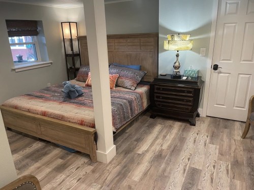Cozy bedroom featuring a wooden bed, colorful bedding, nightstand, lamp, and warm wood flooring.