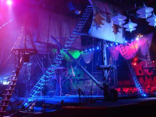 A colorful circus stage featuring a pirate ship with ropes, ladders, and vibrant lighting effects.