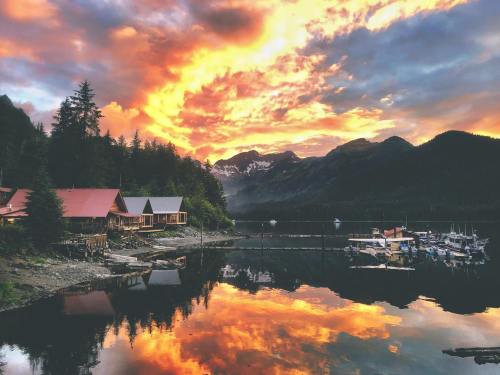 A serene lakeside scene at sunset, with colorful clouds reflecting on the water and mountains in the background.