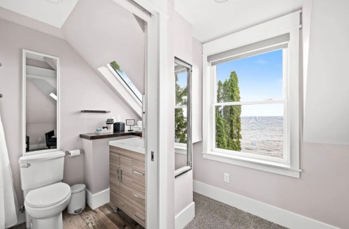 Bright bathroom with a modern vanity, large windows, and a view of the water outside. Light-colored walls and flooring.