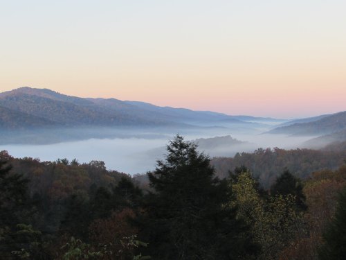 A serene mountain landscape at dawn, with mist rolling through valleys and soft pastel colors in the sky.