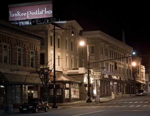 Nighttime view of a quiet street featuring the Yankee Pedlar Inn and historic buildings, illuminated by streetlights.