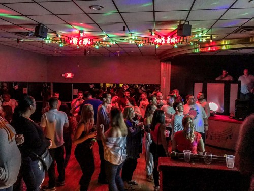 A lively dance floor filled with people enjoying music under colorful lights in a vibrant venue.