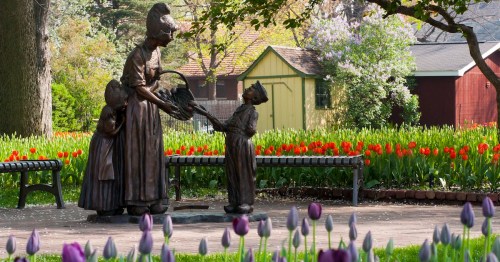 A bronze statue of a woman and two children in a garden filled with colorful tulips and greenery.