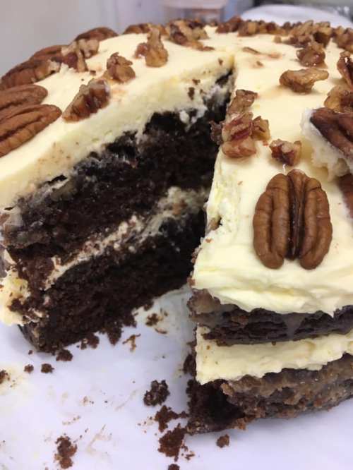 A layered chocolate cake with cream frosting and pecans on top, partially sliced to reveal its rich interior.