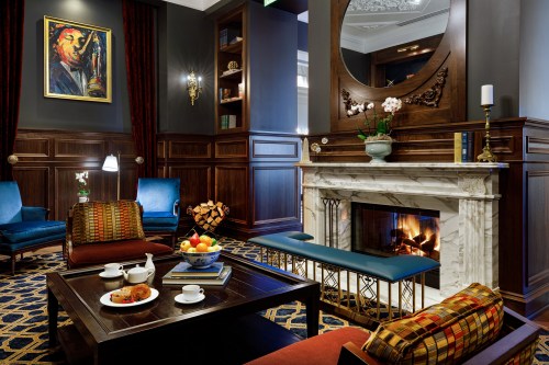 Cozy lounge with a fireplace, elegant seating, a fruit bowl, and artwork on the walls, creating a warm atmosphere.
