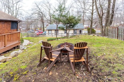 Two wooden chairs around a fire pit in a grassy yard, with trees and a house in the background.