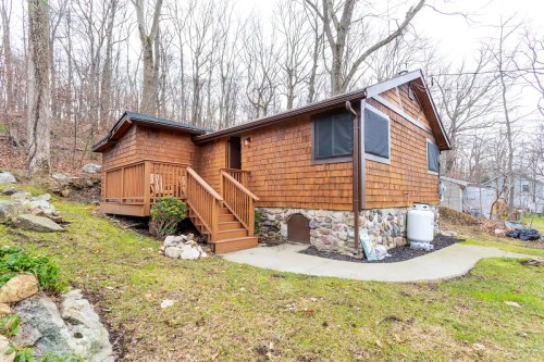 A cozy wooden cabin with stone accents, surrounded by trees and a grassy area, featuring a front porch and steps.
