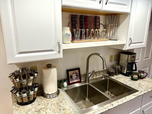 A cozy kitchen with a double sink, coffee maker, and a decorative "WELCOME" sign on the shelf above.