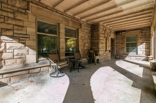A spacious porch with stone walls, featuring chairs and sunlight casting shadows on the floor.