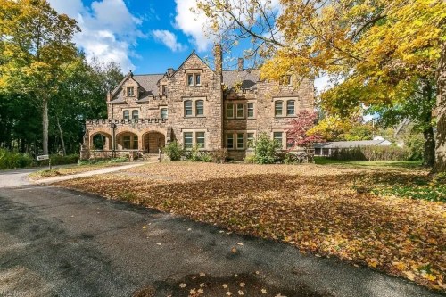 A large, historic stone mansion surrounded by colorful autumn foliage and fallen leaves on the ground.