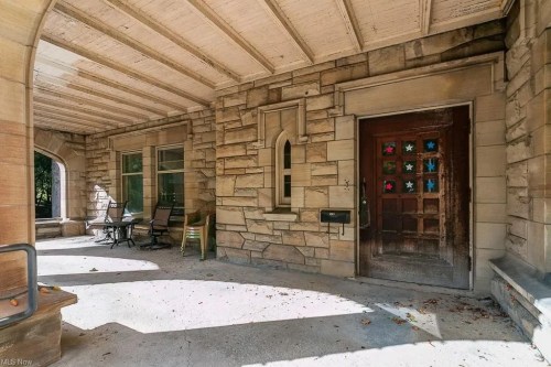 Stone porch with a wooden door featuring colorful star decorations, surrounded by chairs and windows.