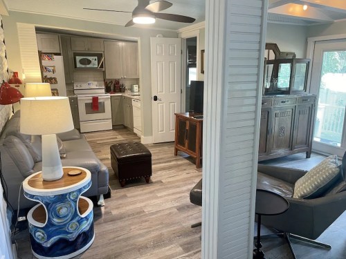 Cozy living space featuring a gray sofa, wooden furniture, and a well-lit kitchen area with modern appliances.