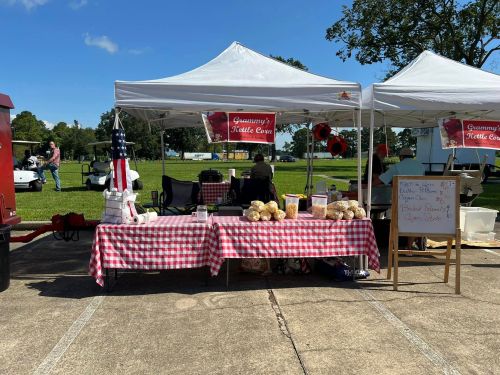 A food stall with a checkered tablecloth, serving popcorn and snacks under a tent at an outdoor event.