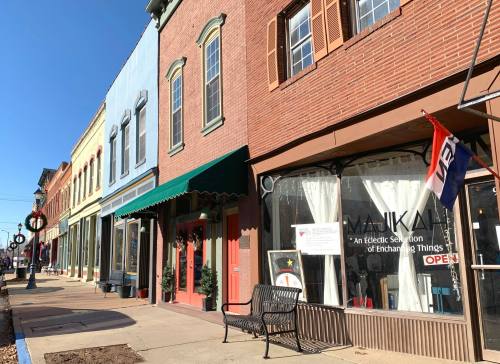 Colorful storefronts line a sunny street, featuring a shop with a sign that says "Open" and festive decorations.