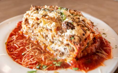 A hearty slice of lasagna topped with cheese and herbs, served on a plate with marinara sauce.