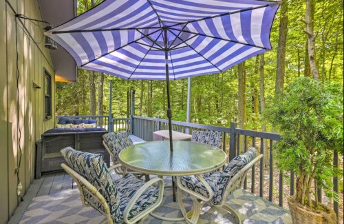 A cozy outdoor patio with a round table, chairs, and a striped umbrella, surrounded by lush green trees.