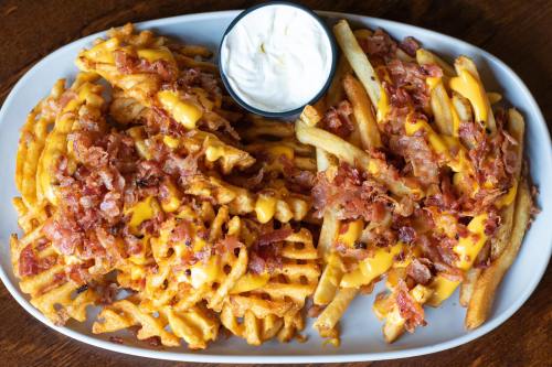 A platter of loaded fries with cheese, bacon bits, and a side of sour cream.