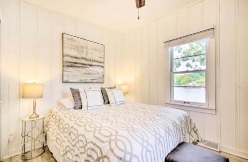 Cozy bedroom with a large bed, decorative pillows, two lamps, and a window overlooking greenery.