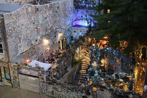 A vibrant, artistic outdoor space with intricate mosaic walls, illuminated pathways, and lively seating areas.