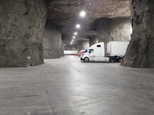 Trucks parked in a large, dimly lit underground cavern with rocky walls and smooth concrete flooring.