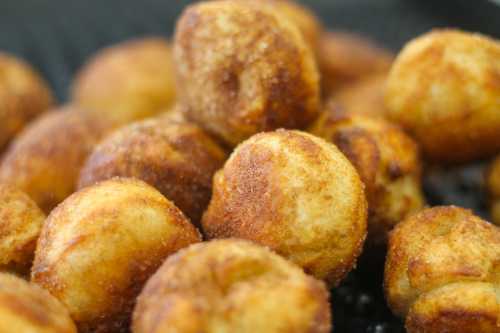 Close-up of golden-brown, crispy dough balls, lightly dusted with cinnamon sugar, piled together.