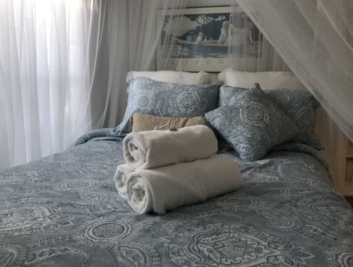 A cozy bed with patterned blue bedding, decorative pillows, and neatly rolled white towels on top.