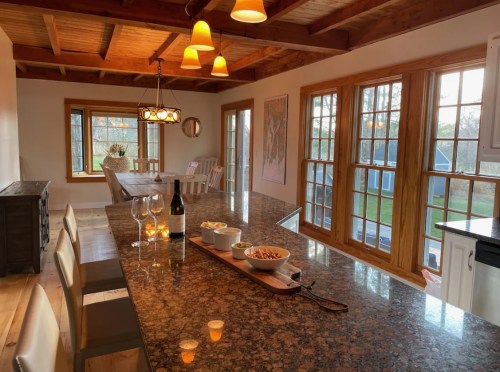 A cozy kitchen with a granite island, wine glasses, snacks, and large windows letting in natural light.