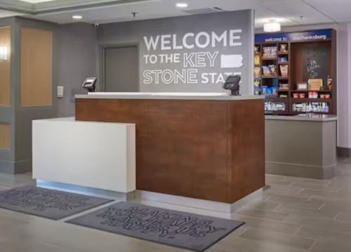 Modern reception area with a wooden front desk and a welcoming sign, featuring snacks and drinks in the background.