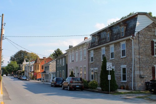 A quiet street lined with historic buildings and parked cars under a clear blue sky.