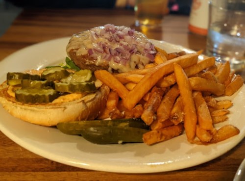 A plate with a burger topped with onions, pickles, and a side of crispy fries.