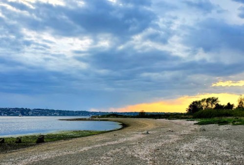 A serene beach scene at sunset, with a cloudy sky and calm water reflecting the fading light.