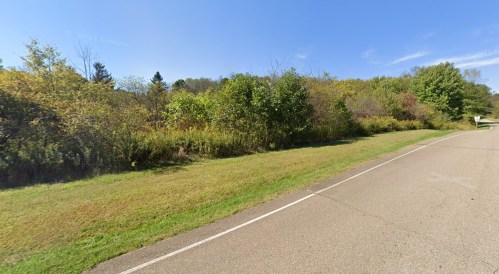 A peaceful roadside scene with green grass, trees, and a clear blue sky.