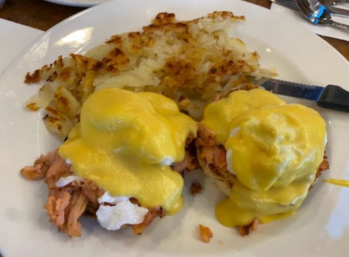 A plate of eggs Benedict with smoked salmon, topped with hollandaise sauce, served with crispy hash browns.